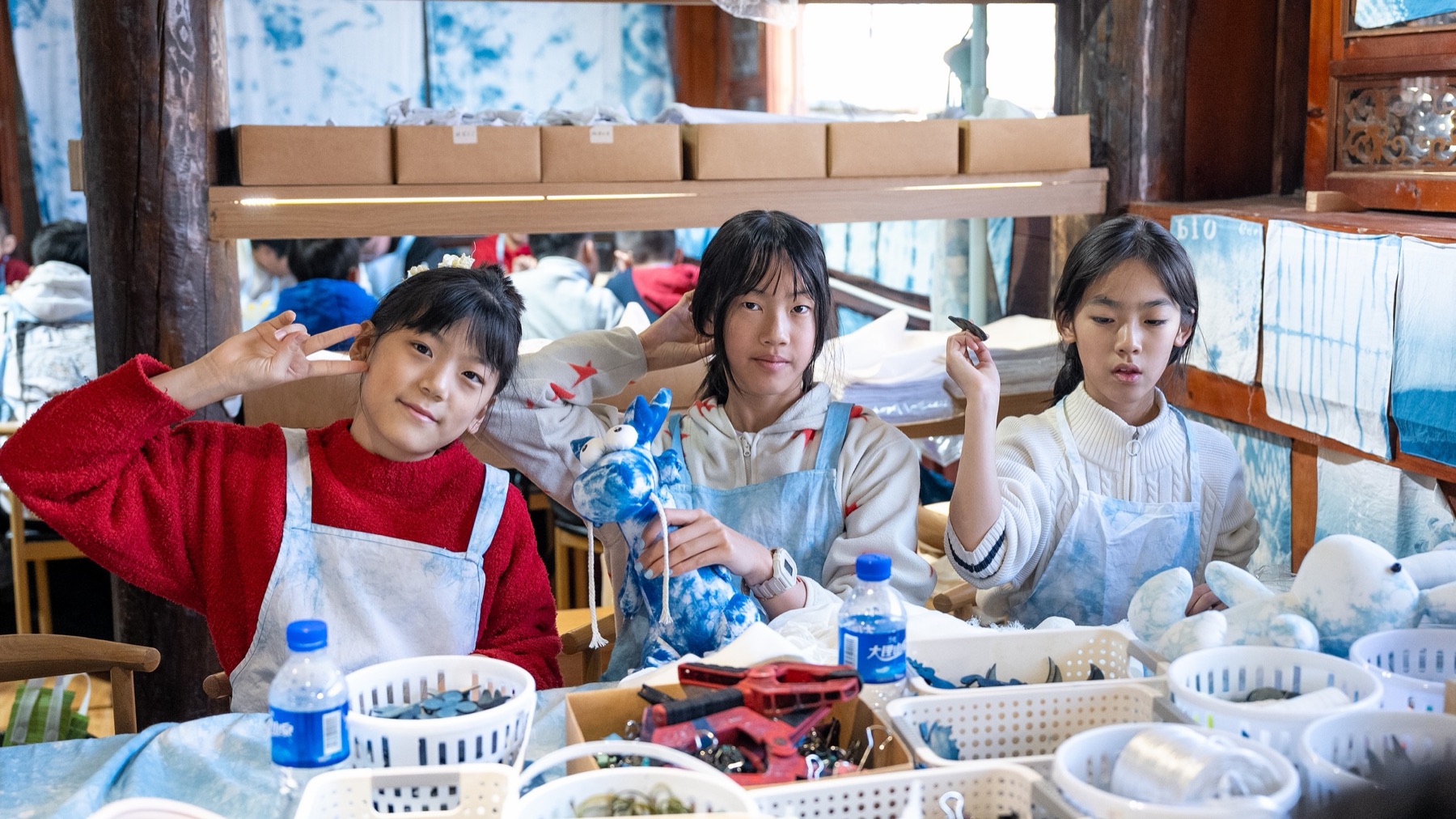 三个孩子围坐在手作桌前，展示蓝白色的布艺作品