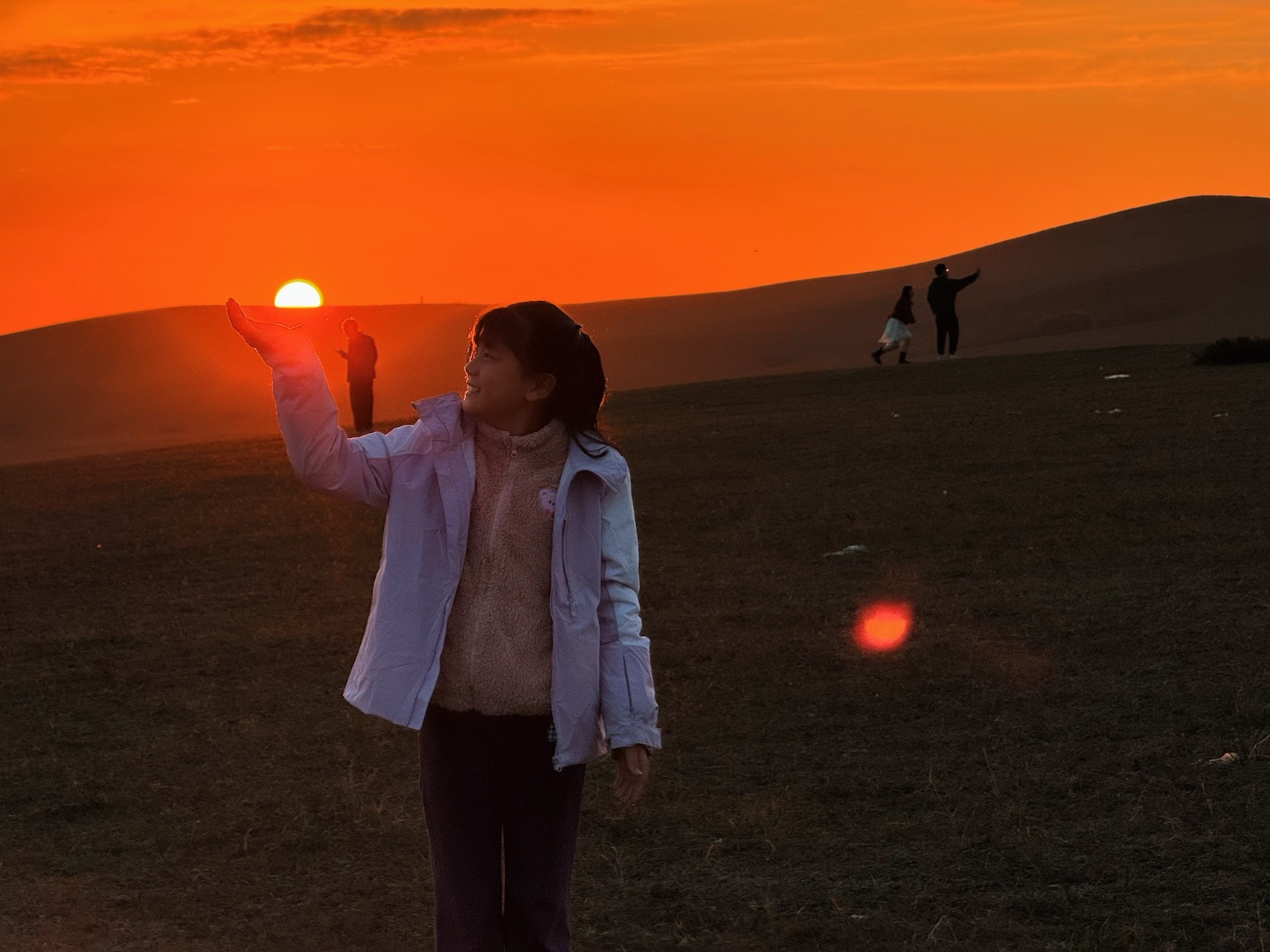 女孩站在橙色夕阳下，伸手做出托起太阳的姿势